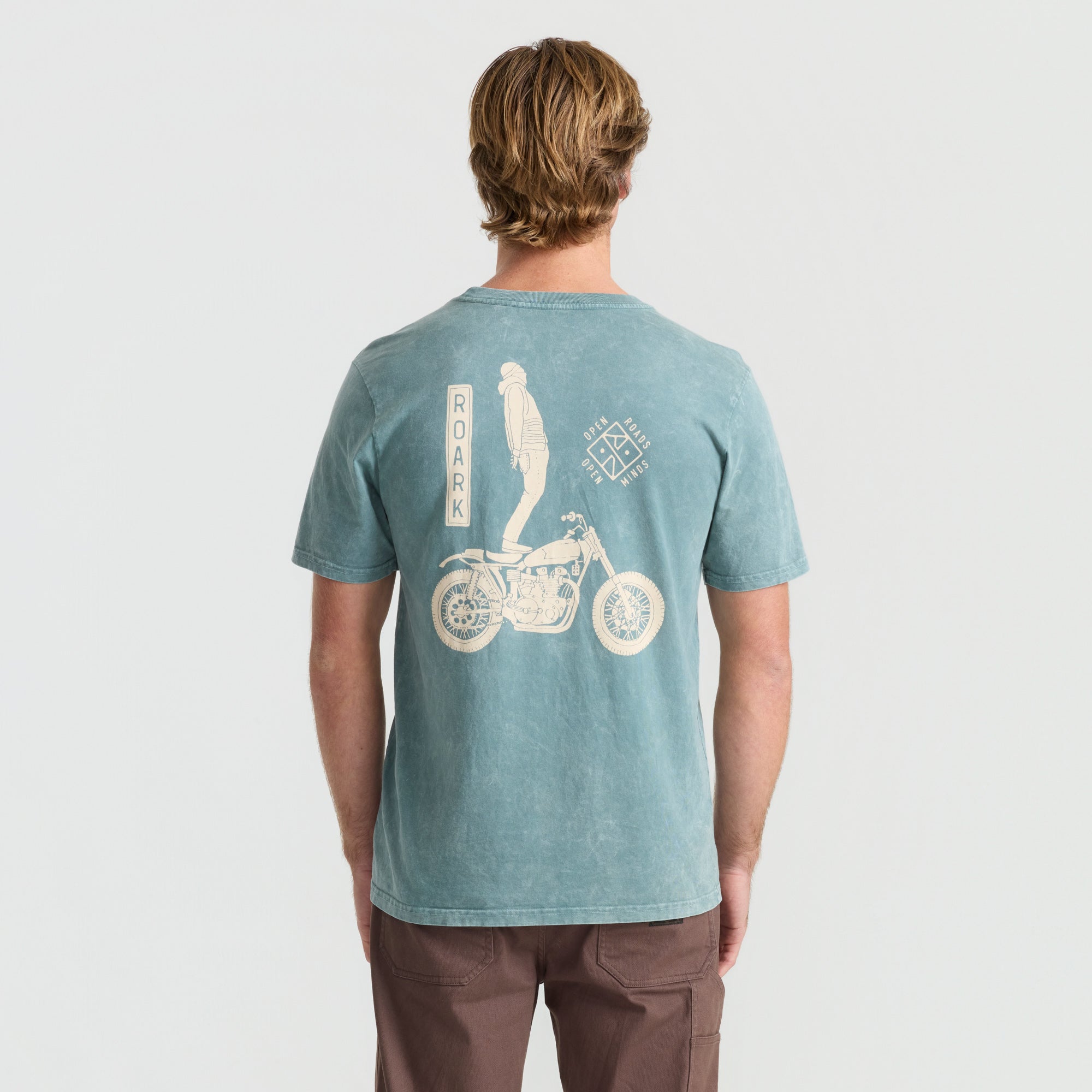 Active cyclist in motion wearing Roark adventure shirt with a detailed bicycle frame in a natural setting.