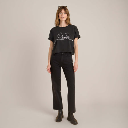 Frau in einem schwarzen, kurzen, grafischen T-Shirt, schwarzen Jeans mit hoher Taille und Ankle Boots, gestylt für einen lässigen und kantigen monochromen Look.